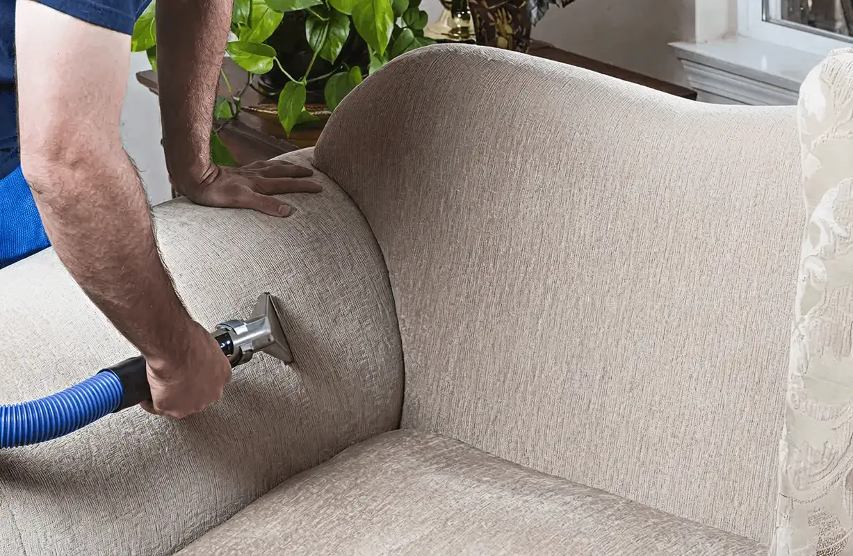 Professional upholstery cleaner deep-cleaning a fabric sofa with a handheld extraction tool and hose, Minneapolis, MN.
